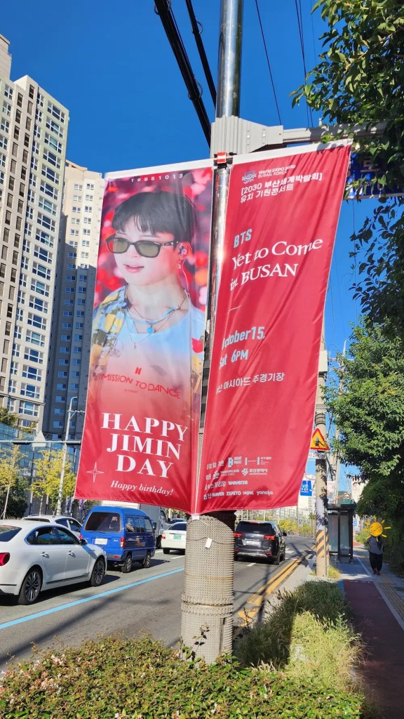 	Daytime banner saying “HBD Jimin” near Cafe Magnate in Busan, celebrating BTS Jimin’s birthday