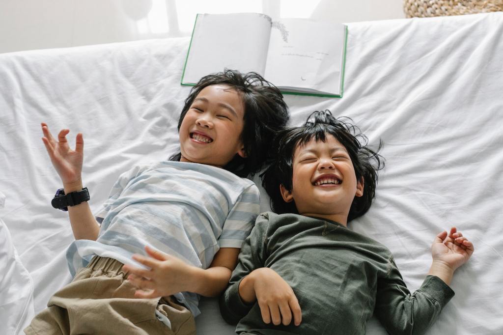 Deux frères coréens allongés sur un lit, riant aux éclats