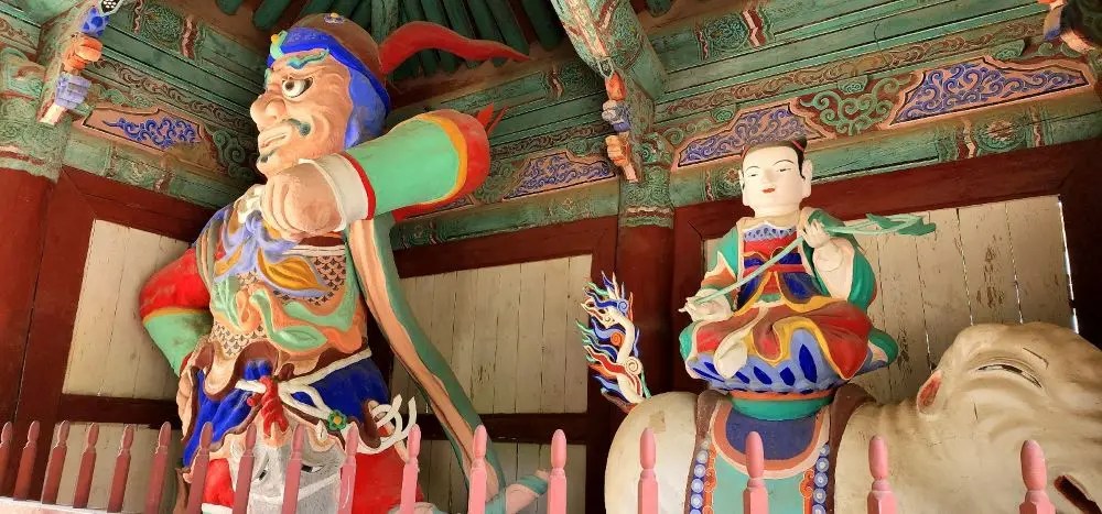 Colorful Korean Buddhist guardian statues inside the gate of Magoksa Temple in Gongju, South Korea, featuring detailed painted wooden figures.
