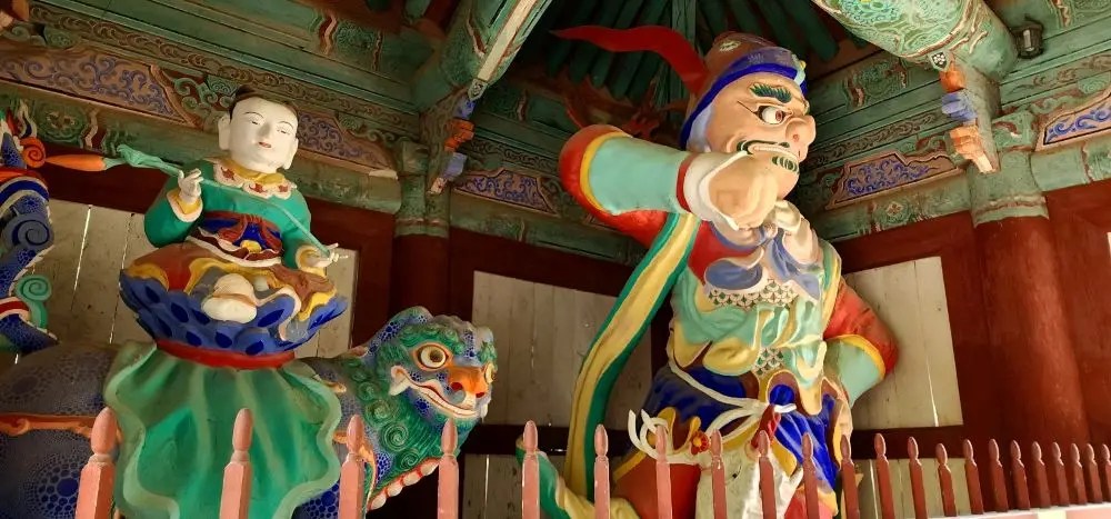 A brightly painted Korean Buddhist guardian statue inside the gate of Magoksa Temple in Gongju, South Korea, with intricate detailing and vivid colors.
