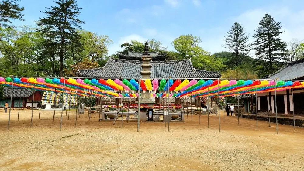 Colorful lantern canopy displayed across the main courtyard of Magoksa Temple in Gongju, South Korea, with a stone pagoda and traditional buildings in the background.