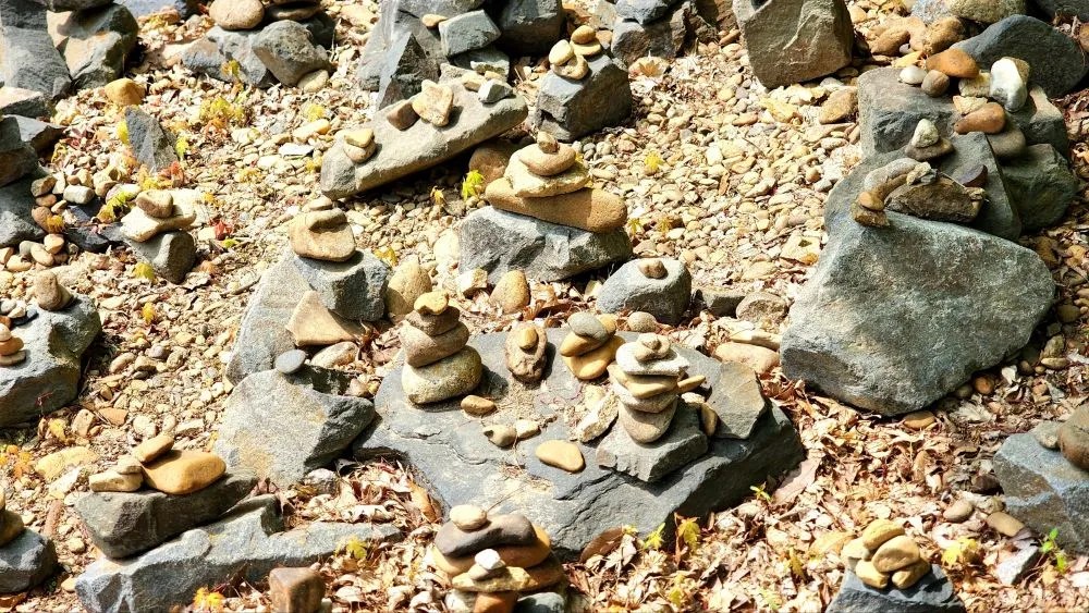A ground area filled with stacked prayer stones at Magoksa Temple in Gongju, South Korea, arranged on rocks and pebbles.