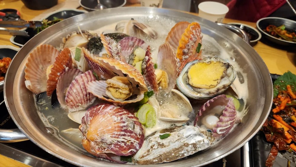 A steaming bowl of Korean seafood kalguksu topped with clams, mussels, and shrimp.