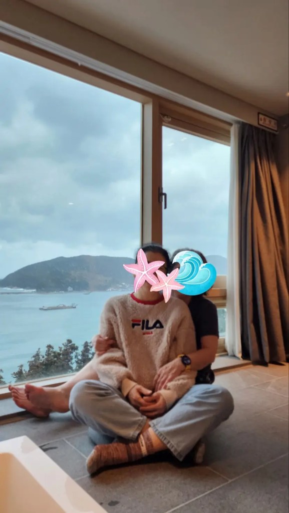 Two women sitting side by side, smiling in front of a scenic hotel view in Geoje.