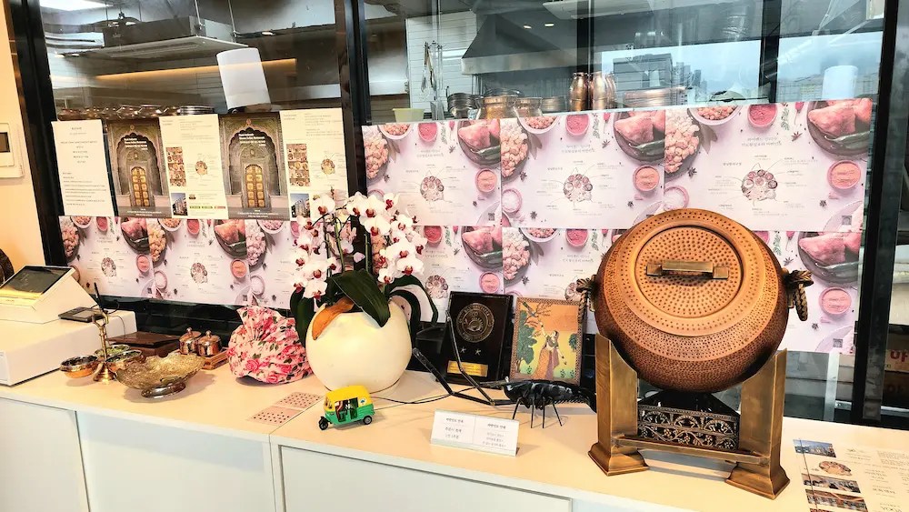 Comptoir décoré avec des objets traditionnels indiens, y compris une jarre, un tuk-tuk miniature et des affiches colorées / Decorated counter with traditional Indian items, including a jar, mini tuk-tuk and colorful posters