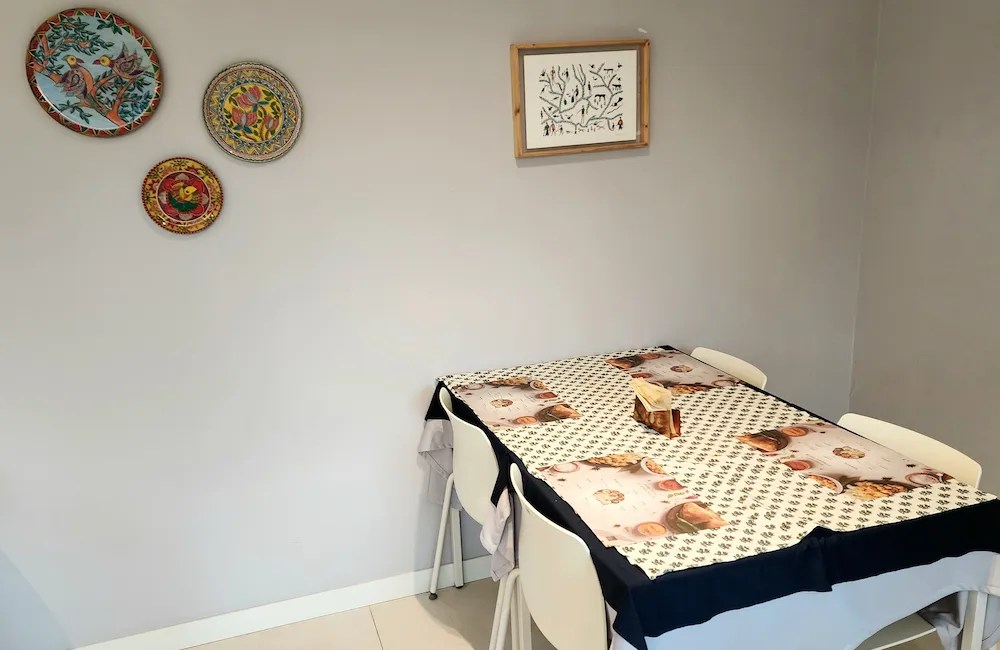 Petite table d’angle avec une nappe à motifs et des assiettes décoratives accrochées au mur / Small corner table with patterned tablecloth and decorative plates on the wall