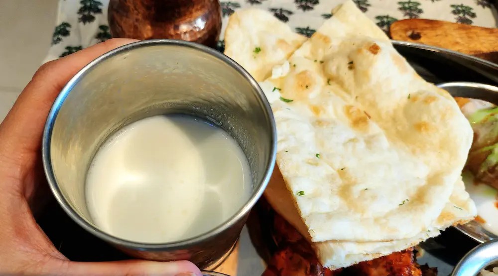 Un verre en métal contenant du lassi sucré indien, tenu dans la main