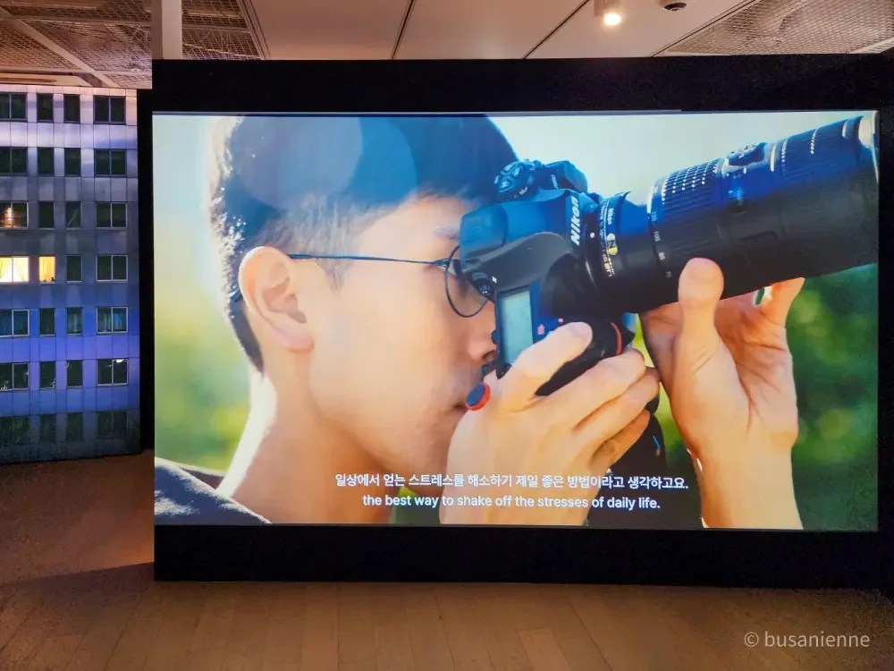Korean photographer Kyungjun Lee holding a Nikon camera while shooting, featured in the “One Step Away” exhibition in Busan 2025