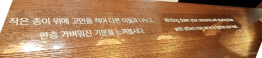 Close-up of a wooden desk with Korean and English text encouraging visitors to write down their concerns and share them with others.