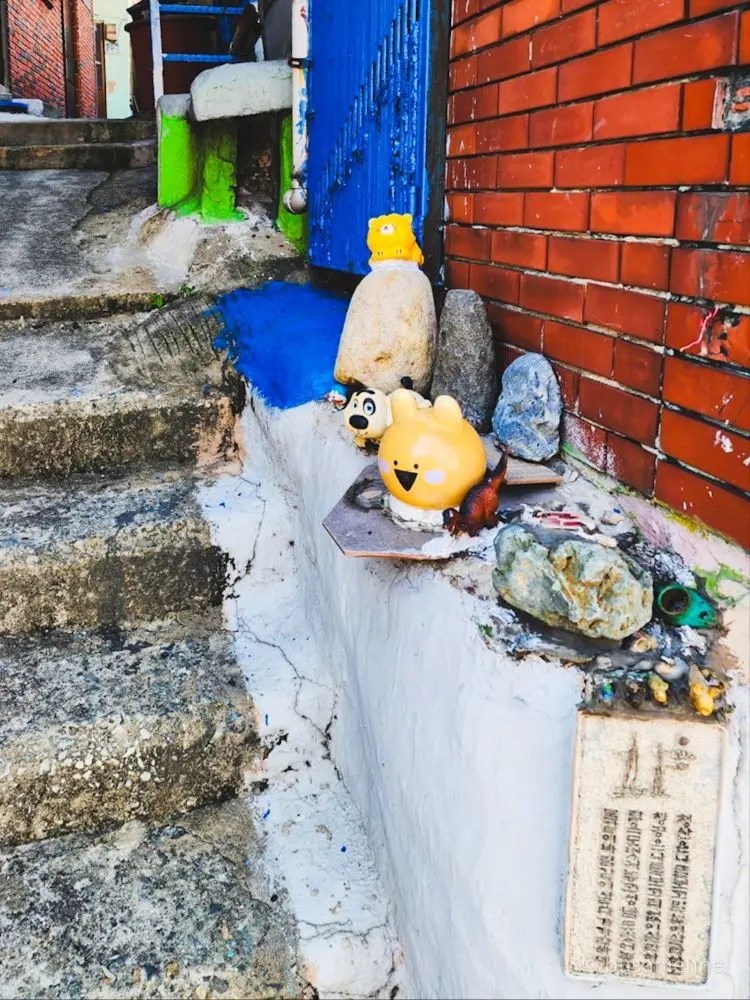 Petit escalier de pierre avec des figurines et décorations devant une maison à Gamcheon Village