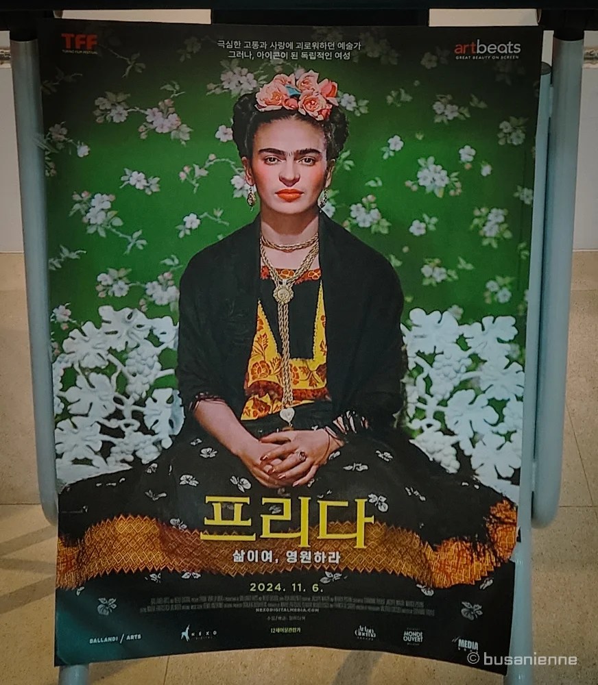 Promotional poster for the documentary 'Frida. Viva La Vida' featuring a portrait of Frida Kahlo with a floral crown, set to premiere on November 6, 2024, connecting with the Frida Kahlo Replica Art Exhibition and cultural Expo in Busan.