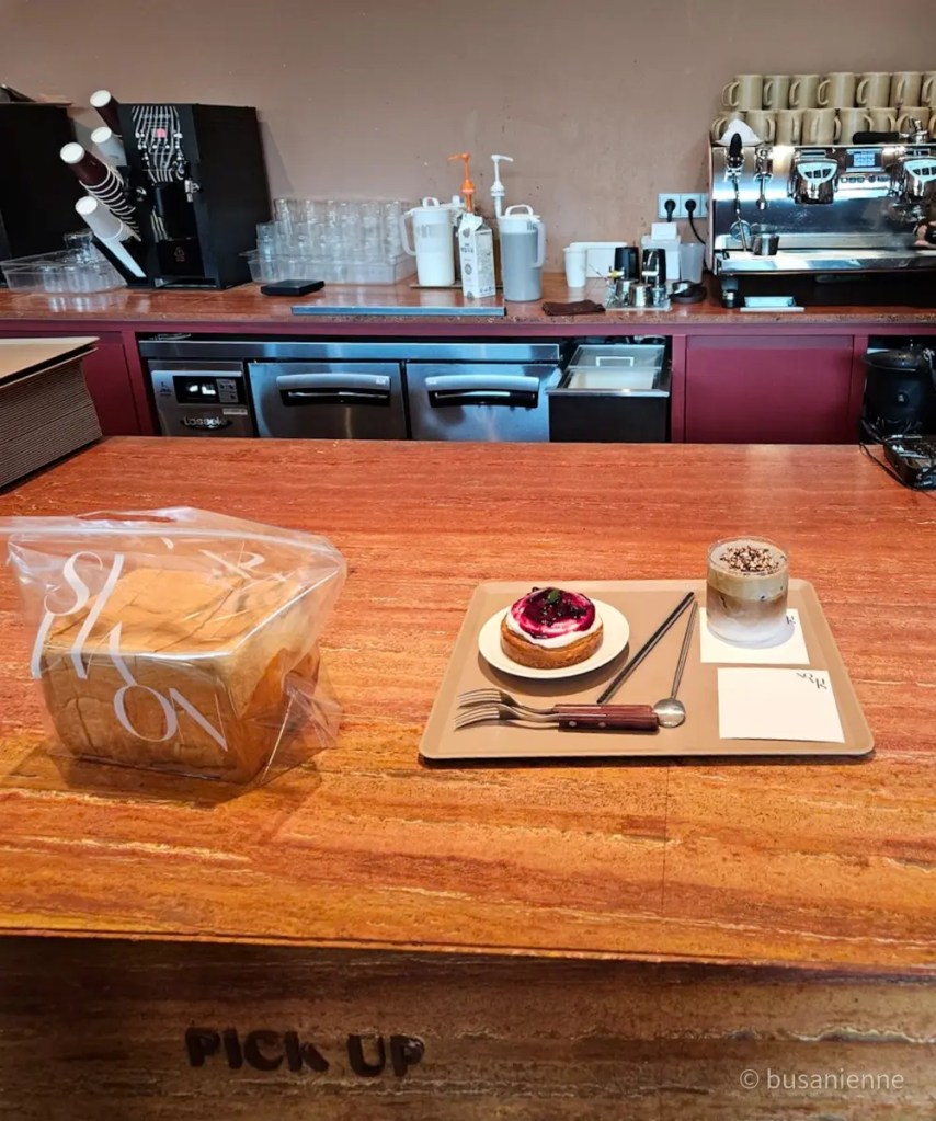 Café counter with berry tart, layered coffee drink, and loaf of bread labeled SHON at Sihaon Café in Ulsan.