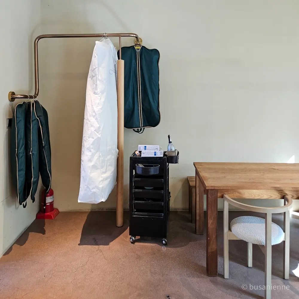 Garment care station with hangers, rolling cart, and wooden table in a minimalist room at Sihaon Café in Ulsan.
