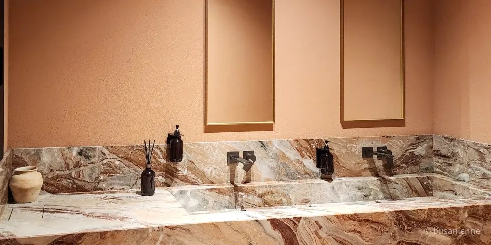 Double marble sink with gold mirrors and black faucets in a peach-toned bathroom at Sihaon Café in Ulsan.