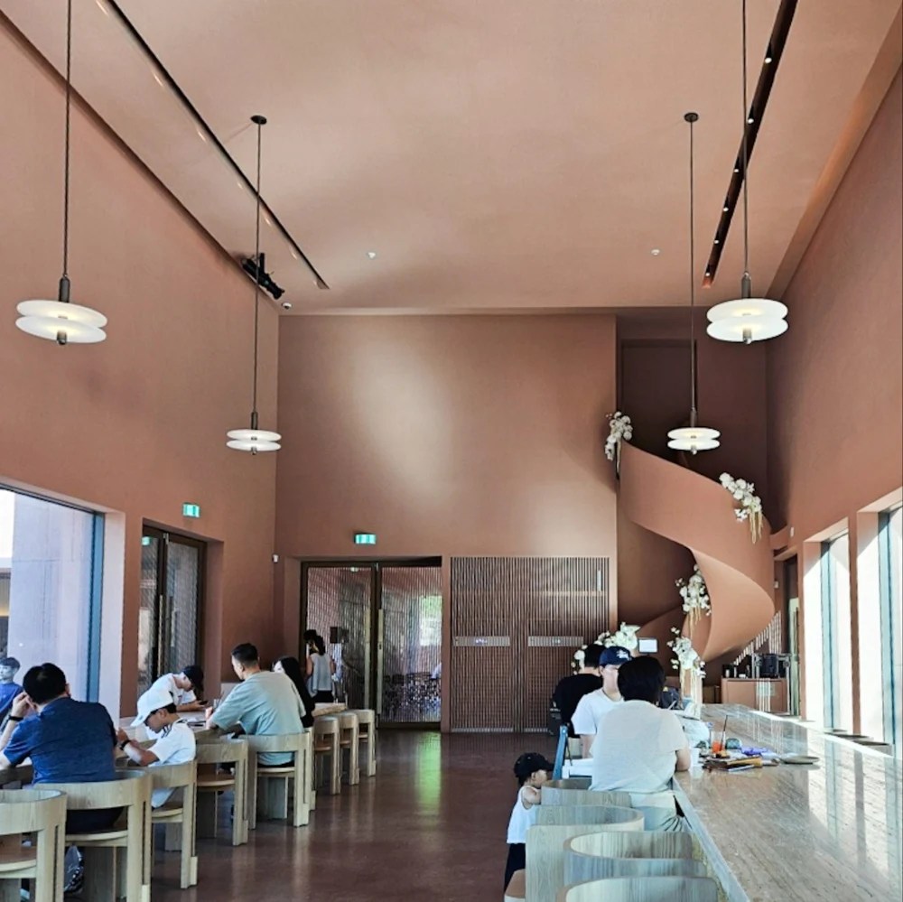 Café interior with spiral staircase, terracotta walls, and communal wooden tables at Sihaon Café in Ulsan.
