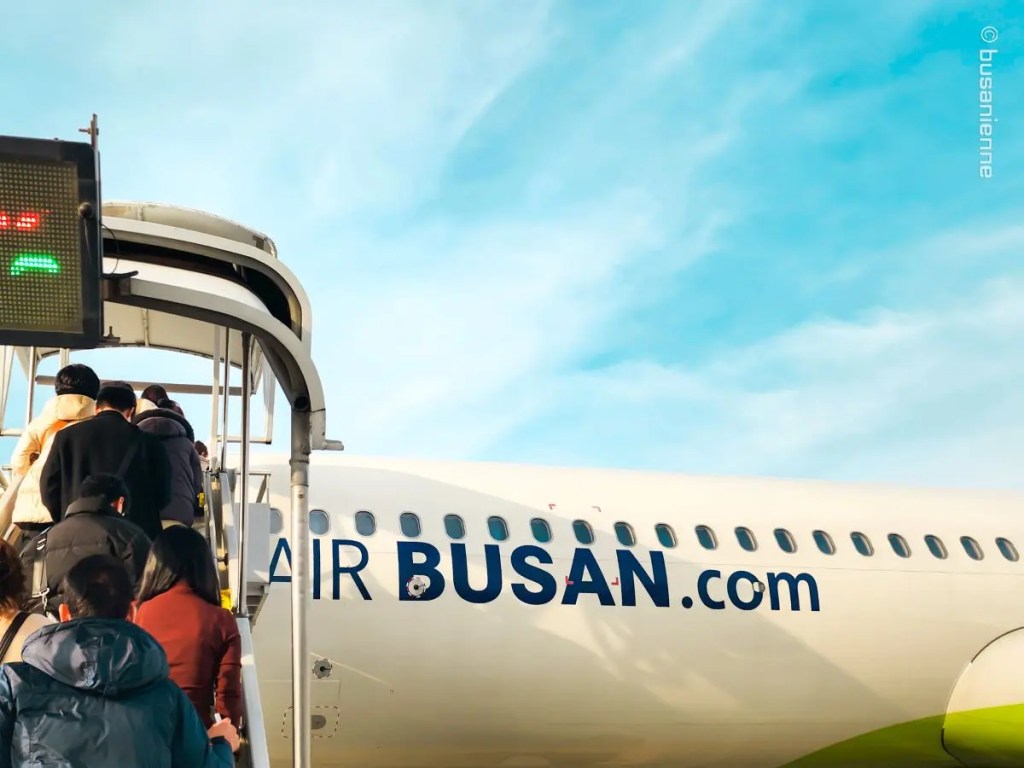 Passengers boarding an Air Busan airplane via stairs under blue sky at airport