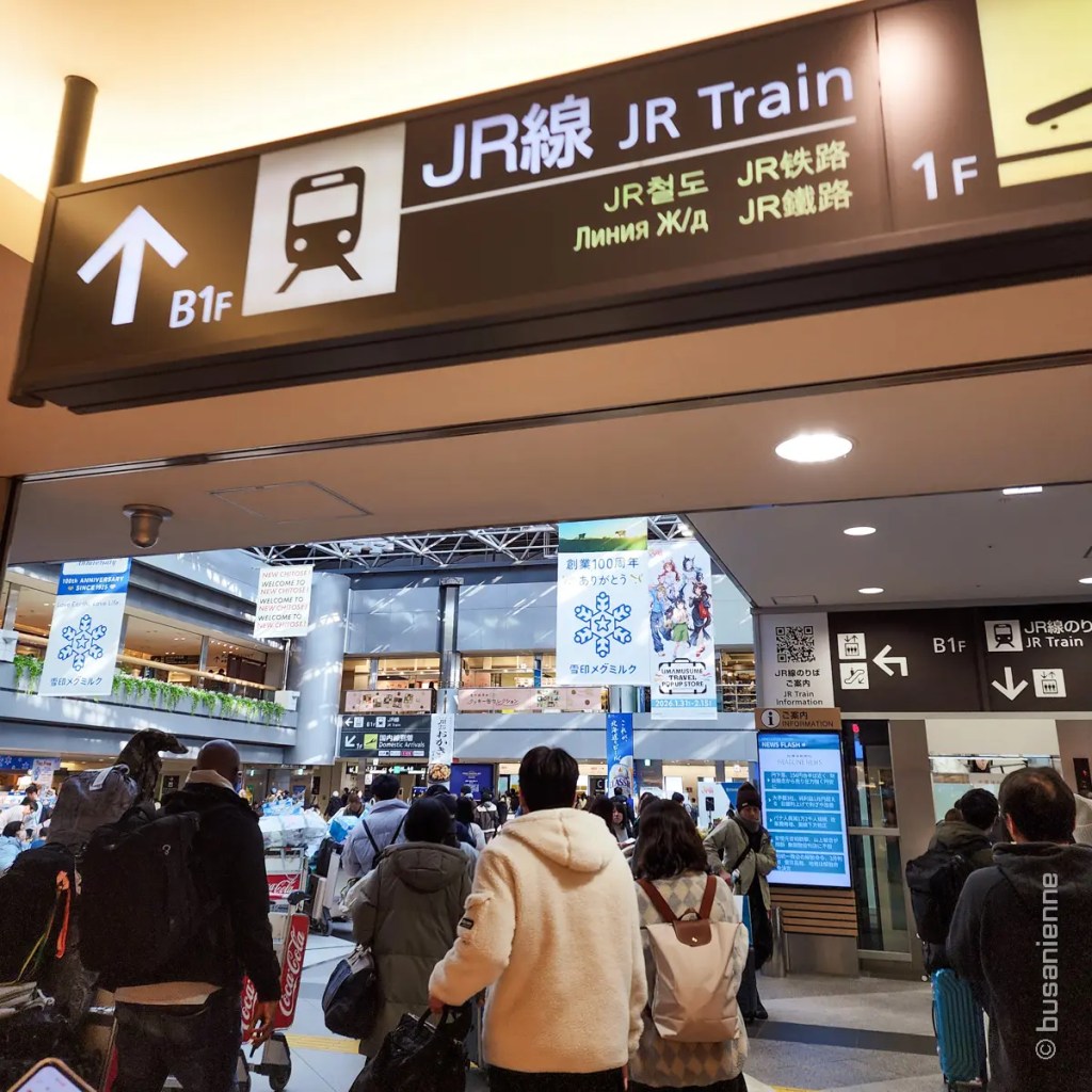JR Train direction sign inside New Chitose Airport with travelers heading to the station in Japan